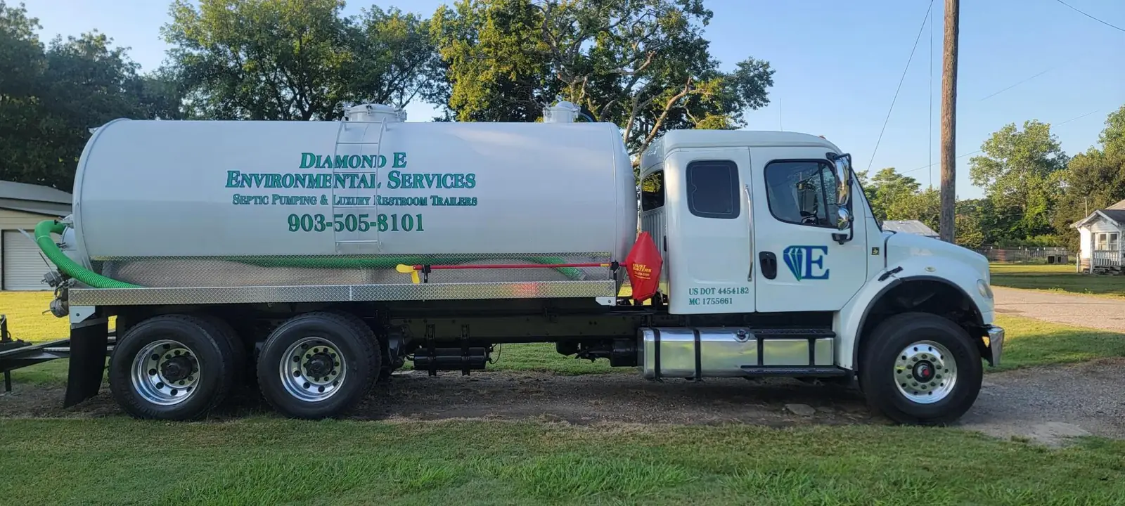 Diamond E Environmental Services white vacuum truck with green hose, lettered Septic Pumping and Luxury Restroom Trailers, 903-505-8101